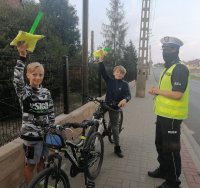 policjant wręcza dzieciom elementy odblaskowe