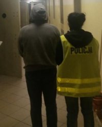 Zatrzymany prowadzony przez korytarz policyjnego aresztu przez policjantkę