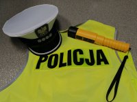 Na zdjęciu widoczna kamizelka odblaskowa z napisem Policja, na kamizelce położona czapka policyjna funkcjonariusza ruchu drogowego oraz urządzenie do badania trzeźwości