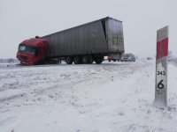 na zdjęciu widoczny pojazd ciężarowy częściowo znajdujący się w rowie, na drodze duża pokrywa śniegu w tle widoczny radiowóz