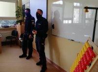 Policjanci w pomieszczeniu klasy szkolnej podczas spotkania z uczniami.