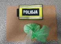 na zdjęciu widoczna torebka foliowa koloru zielonego z zawartością białego proszku, obok opaska z napisem Policja