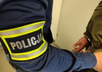 ręka policjanta z opaską policja trzymający zatrzymanego z zapiętymi kajdankami