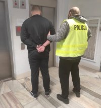 policjant stojący z zatrzymanym przed windą
