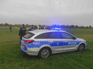 na zdjęciu widać oznakowany policyjny radiowóz stojący na pasie zieleni Aeroklubu Ziemi Piotrkowskeij