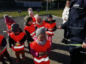 policjant wraz z dzieci, przekazuje im opaski odblaskowe