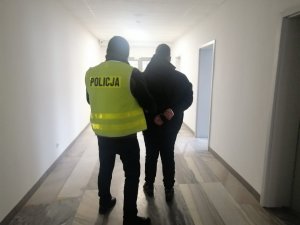 podejrzany z policjantem w kamizelce z napisem policja idący przez korytarz