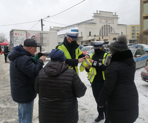 policjant i policjantka ruchu drogowego na miejskim targowisku rozdają kamizelki odblaskowe seniorom