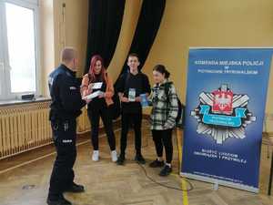 dzielnicowy przekazuje młodzieży ulotki informacyjne na temat procesu rekrutacji do Policji