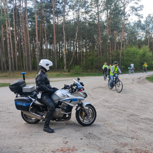funkcjonariusz ruchu drogowego na policyjnym motocyklu czuwa nad bezpiecznym przejazdem uczestników rajdu rowerowego