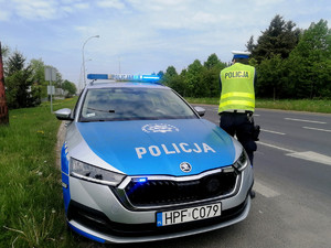 policjant piotrkowskiej drogówki mierzy prędkość jadących pojazdów, na zdjęciu stoi przy oznakowanym radiowozie