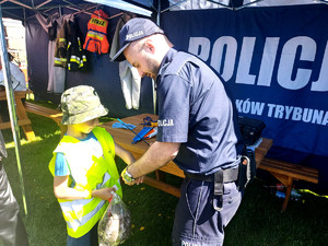 policjant zakłada chłopcu na rękę opaskę odblaskową