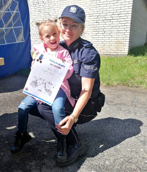 Policjantka trzyma na kolanach dziewczynkę z grupy przedszkolnej podczas pikniku z okazji Dnia Dziecka