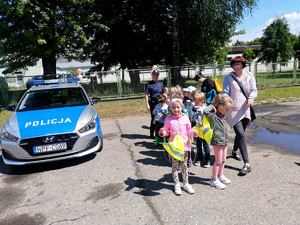 na zdjęciu widać grupę dzieci z przedszkola, policjantkę oraz policyjny radiowóz