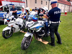 dwaj chłopcy siedzą na motocyklach policyjnych, obok stoi policjant
