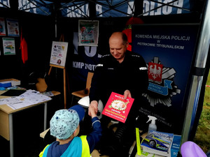policjant stojący w policyjnym namiocie przekazuje chłopcu nagrodę w postaci książki