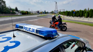 policyjne sygnały świetlne na radiowozie, w tle motocyklista