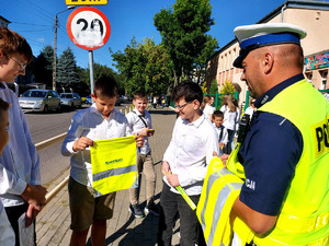 Policjant ruchu drogowego przed budynkiem piotrkowskiej podstawówki rozdaje uczniom elementy odblaskowe