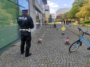policjant ruchu drogowego przygląda się pokonywaniu toru przeszkód przez młodego rowerzystę