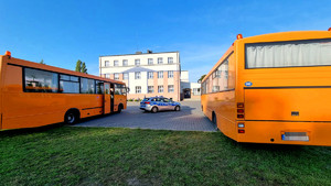 policyjny radiowóz pomiędzy szkolnymi autobusami, w tle widać budynek Szkoły Podstawowej w Wolborzu