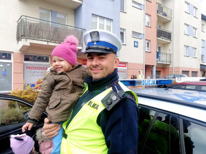 policjant piotrkowskiej drogówki trzyma na rękach dziewczynkę z grupy przedszkolnej podczas wizyty w przedszkolu