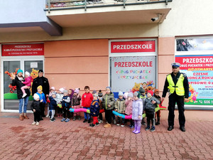 Dzieci oraz policjanci stoją przed budynkiem przedszkola