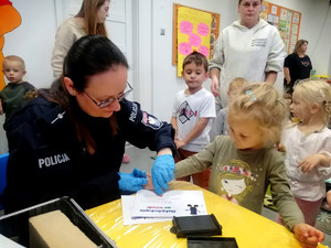 daktyloskopia na wesoło, na zdjęciu policjantka pokazuje dzieciom jak zrobić odcisk linii papilarnych