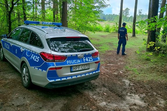 na zdjęciu policyjny radiowóz i policjant stojący na skraju lasu.