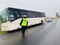 na zdjęciu widać policjanta ruchu drogowego w umundurowaniu stojący obok autokaru, który prawym kołem zjechał w dół melioracyjny