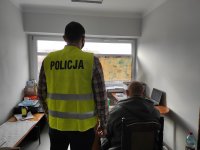 zatrzymany siedzi na krześle podczas przesłuchania, obok niego stoi policjant
