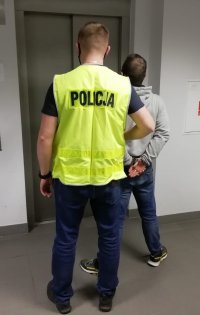 policjant z zatrzymanym stoją przed windą