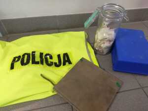 na zdjęciu widać policyjną kamizelkę,a przy niej słoik z dilerkami , notatnik, plastikową niebieską apteczkę zabezpieczone przez policjantów