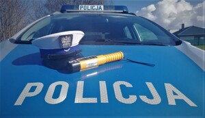 na zdjęciu widać policyjną czapkę na masce oznakowanego radiowozu i leżący obok alkomat