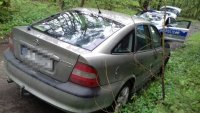 na zdjęciu widać na oierwszym planie samochód osobowy w kompleksie leśnym, w tle oznakowany policyjny radiowóz