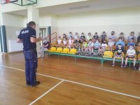 na zdjęciu widać policjanta przeprowadzającego pogadankę z najmłodszymi uczniami szkoły podstawowej. Miejsce przedsięwzięcia to sala gimnastyczna Szkoły Podstawowej w Milejowie