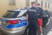policjant prowadzi zatrzymanego do policyjnego radiowozu