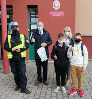 policjant,przedstawiciele piotrkowskiego WORD-u oraz uczniowie  stoją przed budynkiem szkoły
