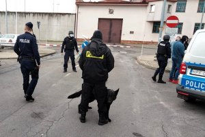 policjanci prowadzą  do radiowozu zatrzymanego przez nich  sprawcę podpalenia budynków aresztu śledczego