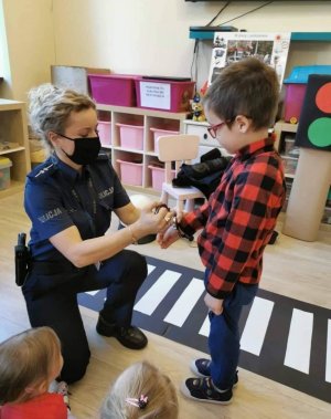 policjantka pokazuje przedszkolakowi jak działają policyjne kajdanki