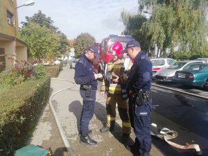 policjanci podczas rozmowy ze strażakiem, z prawej strony widoczne wozy strażackie