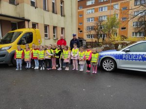dzieci ubrane w kamizelki odblaskowe przed przedszkolem razem z policjantem i przedstawicielem grupy Kierowcy Dzieciom