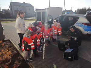 milusińscy stojący obok radiowozu, z prawej strony policjant tłumaczy w jaki sposób działa urządzenie do pomiaru trzeźwości