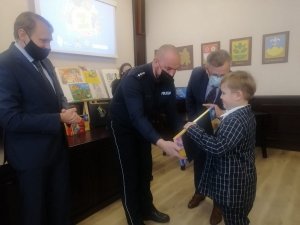 policjant wręcza nagrodę i dyplom laureatowi konkursu plastycznego