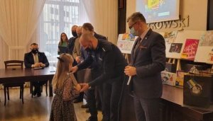 policjant wręcza nagrodę laureatce konkursu plastycznego ,, Wiem, co zrobić&quot;