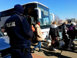 policjant zabezpieczający przyjazd uchodźców w tle autokar