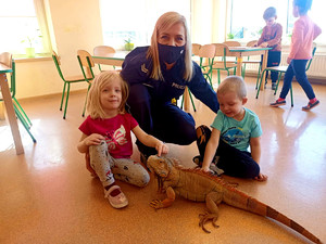 policjantka z dziećmi, przed nimi na podłodze stoi legwan