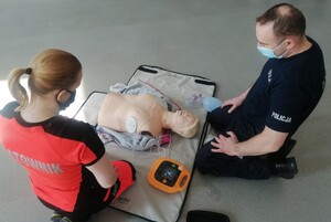 policjant i ratownik podłączają automatyczny defibrylator podczas szkolenia z pierwszej pomocy