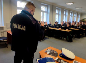 policjant podczas przeprowadzonej pogadanki w szkole, w tle uczniowie siedzący w ławkach