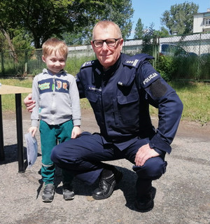Komendant Miejski Policji w Piotrkowie Trybunalskim pozuje do zdjęcia z chłopcem z grupy przedszkolnej podczas pikniku z okazji Dnia Dziecka