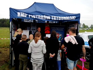 odwiedzający stoją przy policyjnym namiocie